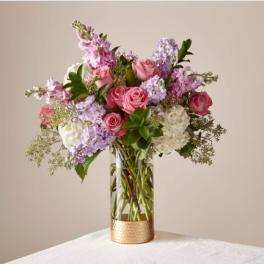 Pink and lavender flower arrangement in a glass vase with a gold base