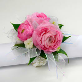 Pink ranunculus wrist corsage with white accent flowers and sheer ribbon on a pearl bracelet.