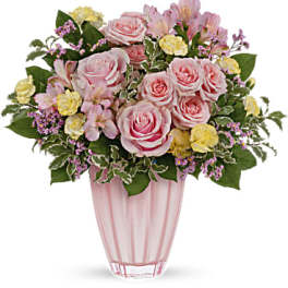 Pink and yellow bouquet of roses and mixed flowers in a pink glass vase