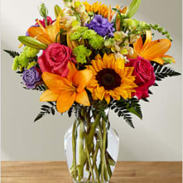Colorful bouquet of lilies, roses, and a sunflower in a clear glass vase