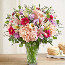 Mixed bouquet of pink lilies, hydrangeas, gerbera daisies, and calla lilies in a glass vase