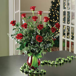 Red roses arranged in a red vase with a green ribbon