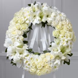 White floral wreath with roses and lilies on a ribboned stand