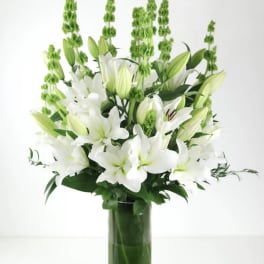 White lilies and green spikes arranged in a tall glass vase