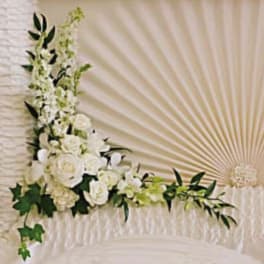 White floral spray arranged on a draped casket with greenery