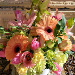Bouquet of peach gerbera daisies, pink lilies, and pale green blooms in a white vase