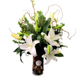 Tall arrangement of white lilies with buds and curly branches in a clear glass vase