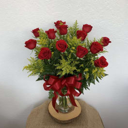 Red roses arranged in a glass vase with a red ribbon