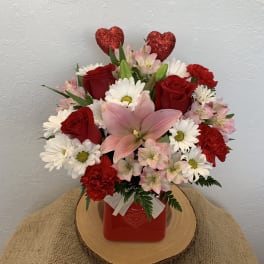 Bouquet of red roses, pink lilies, and white daisies in a red vase with heart picks