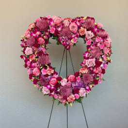 Heart-shaped floral wreath on a stand with pink and purple flowers