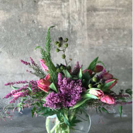 Pink tulips and purple flowers arranged in a clear glass vase
