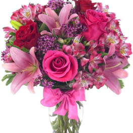Pink and red mixed bouquet in a clear glass vase with a pink ribbon