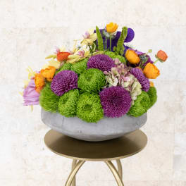 Colorful flower arrangement in a gray bowl vase on a gold stand
