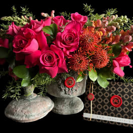 Hot pink roses and orange pincushion blooms in a stone vase with a patterned card