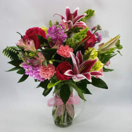 Mixed bouquet of pink and red flowers in a glass vase with a pink ribbon