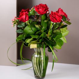 Red roses arranged in a clear glass vase with green foliage