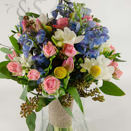 Mixed bouquet of pink, white, and blue flowers in a glass vase