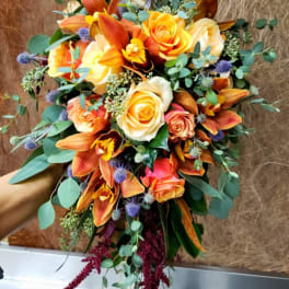 Bouquet of orange and cream roses with orange orchids and blue thistle