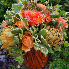Orange and pink roses in a woven basket with variegated ivy