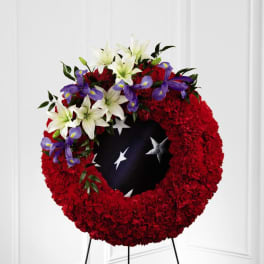 Red floral funeral wreath with white lilies and purple flowers on a stand