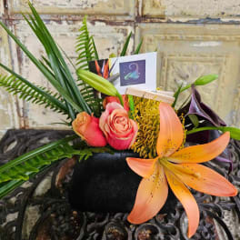 Tropical floral arrangement with roses, lilies, and a Scorpio card in a black container