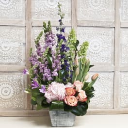 Tall mixed bouquet with roses, tulips, and purple spikes in a gray vase