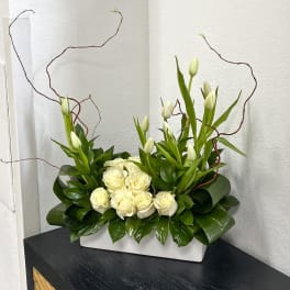 White roses and tulips arranged in a rectangular vase with curly branches
