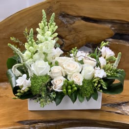 White roses and snapdragons arranged in a white rectangular vase