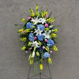 Standing floral spray with white lilies, blue hydrangeas, and yellow snapdragons