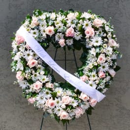 Heart-shaped floral wreath with pink roses and white daisies on a stand