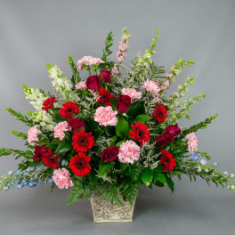 Mixed bouquet of red roses, pink carnations, and red daisies in a decorative vase