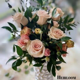 Blush roses arranged in a textured white vase with dark foliage