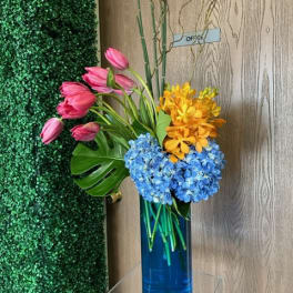 Pink tulips with blue and yellow flowers in a tall blue vase