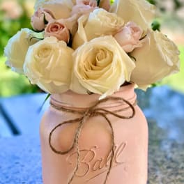 Cream and blush roses arranged in a pink mason jar vase