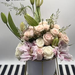 Blush roses and pink lilies arranged in a white vase with tall buds