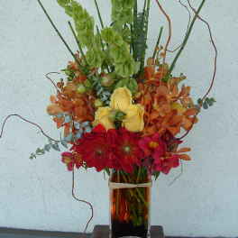 Tall mixed bouquet in a glass vase with red, yellow, orange, and green flowers