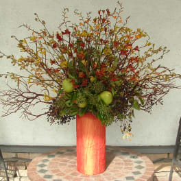 Tall autumn floral arrangement in a red vase with apples