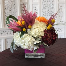 Mixed bouquet with hydrangeas, roses, and lilies in a square glass vase