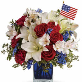 Red roses and white lilies in a blue vase with a small American flag