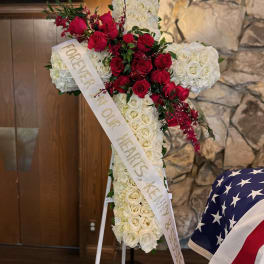 Cross-shaped floral tribute of red and white roses with a memorial ribbon