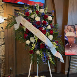 Standing floral tribute with red and white roses and a white ribbon reading "We salute you"