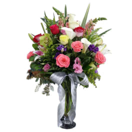 Mixed bouquet of roses, calla lilies, and orchids in a glass vase with a silver ribbon