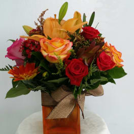 Mixed bouquet of roses, lilies, and a gerbera daisy in an orange vase