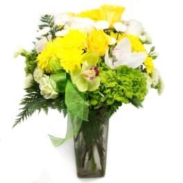Yellow and white floral arrangement in a glass vase with a green ribbon