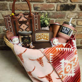 Gift basket with a patterned tote, tumblers, candles, a cap, and folded blankets