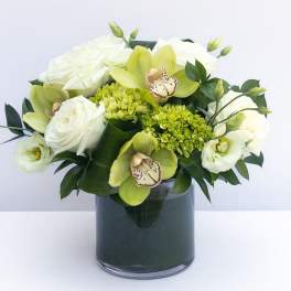 White roses and green orchids arranged in a dark glass vase