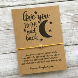 A card with a yellow string bracelet and moon graphic on a wood surface