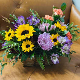 Mixed bouquet with sunflowers, purple blooms, and pink carnations in a basket