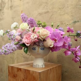 Pink and lavender flowers arranged in a face-shaped vase