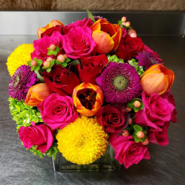 Bright mixed bouquet of roses, tulips, and mums in a square glass vase